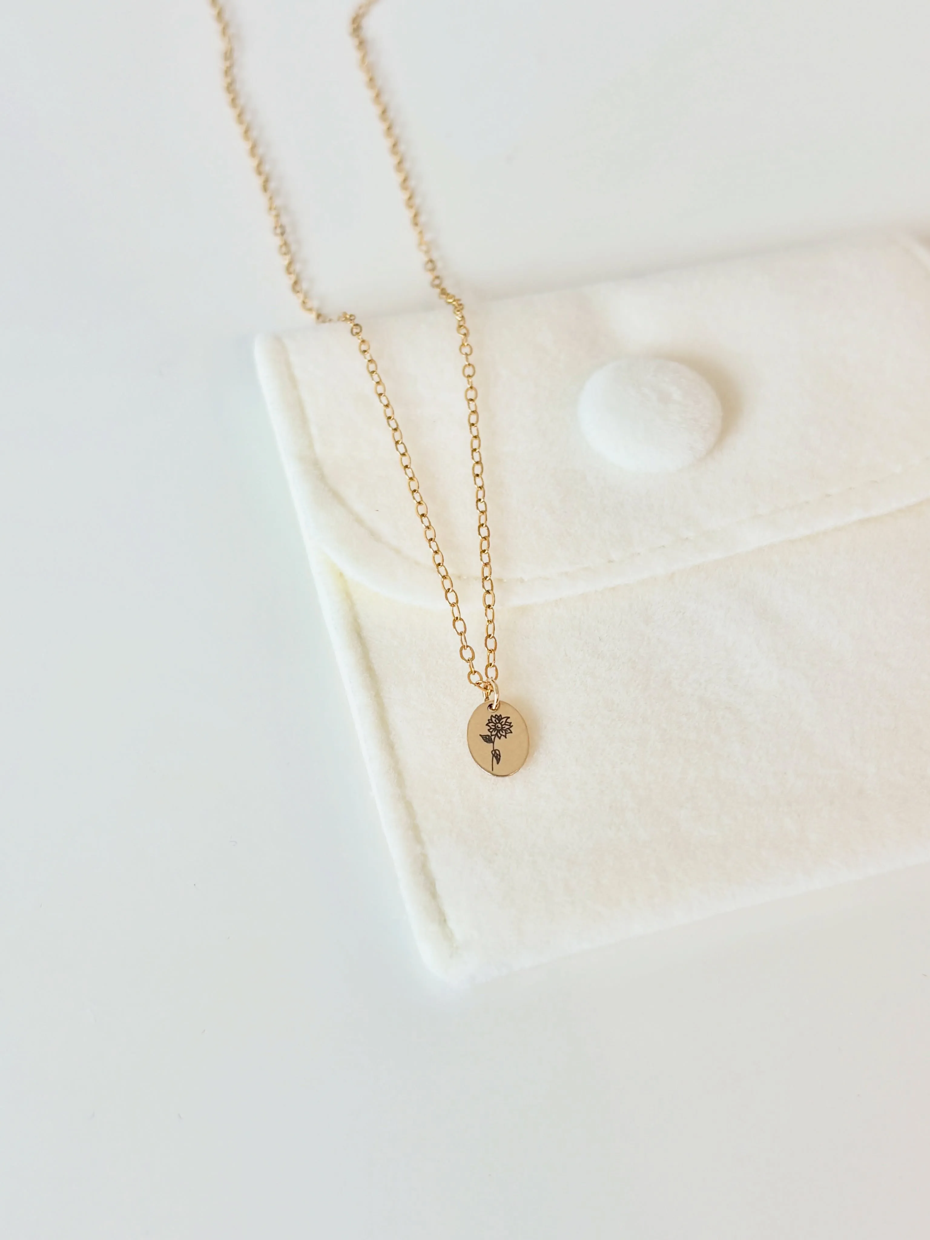 Hand-engraved sunflower necklace on an ivory velvet pouch