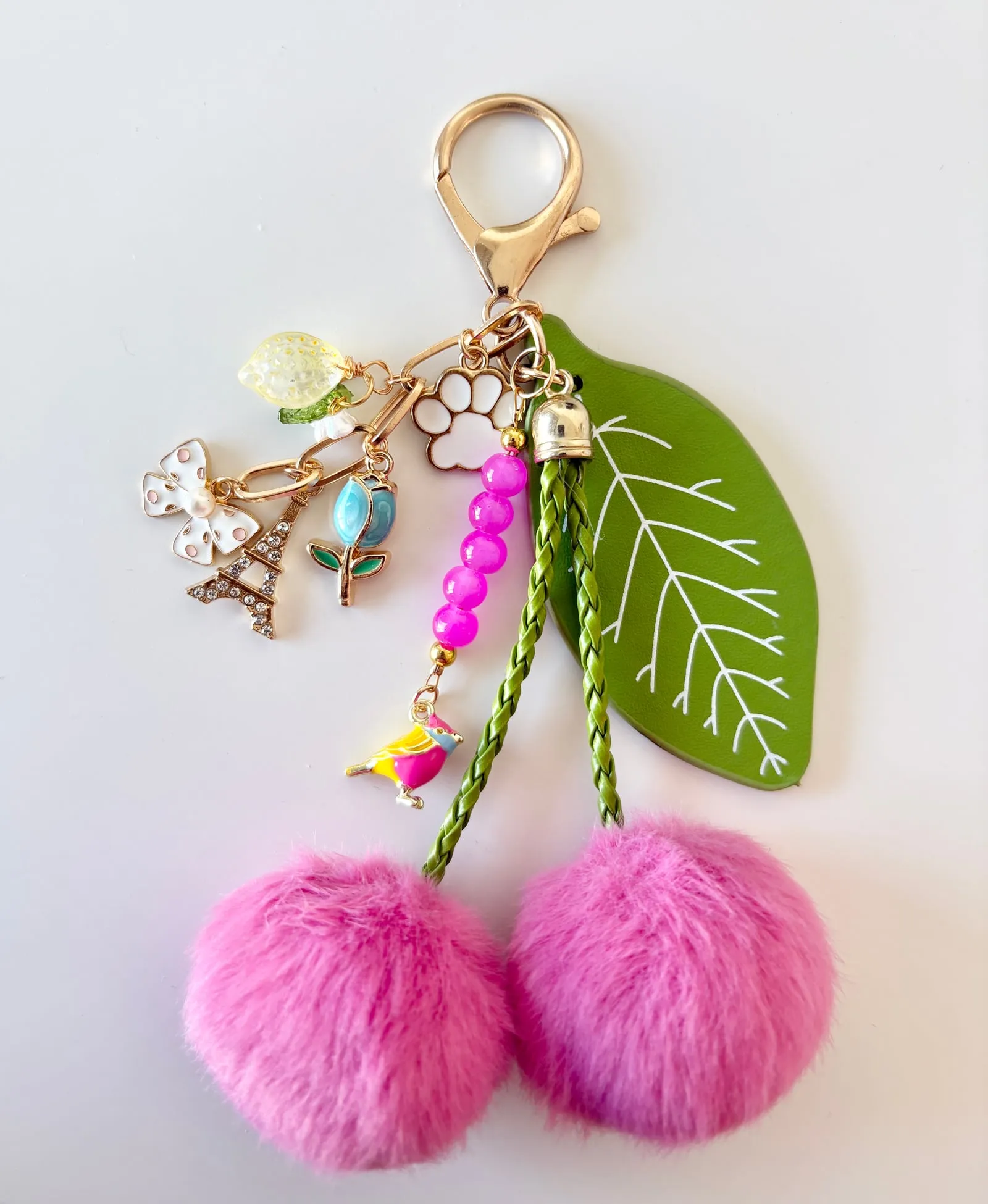 A colourful purse charm keychain with pink pom-poms, enamel charms and a leather leaf tag, made by Dirty Bird Jewellery